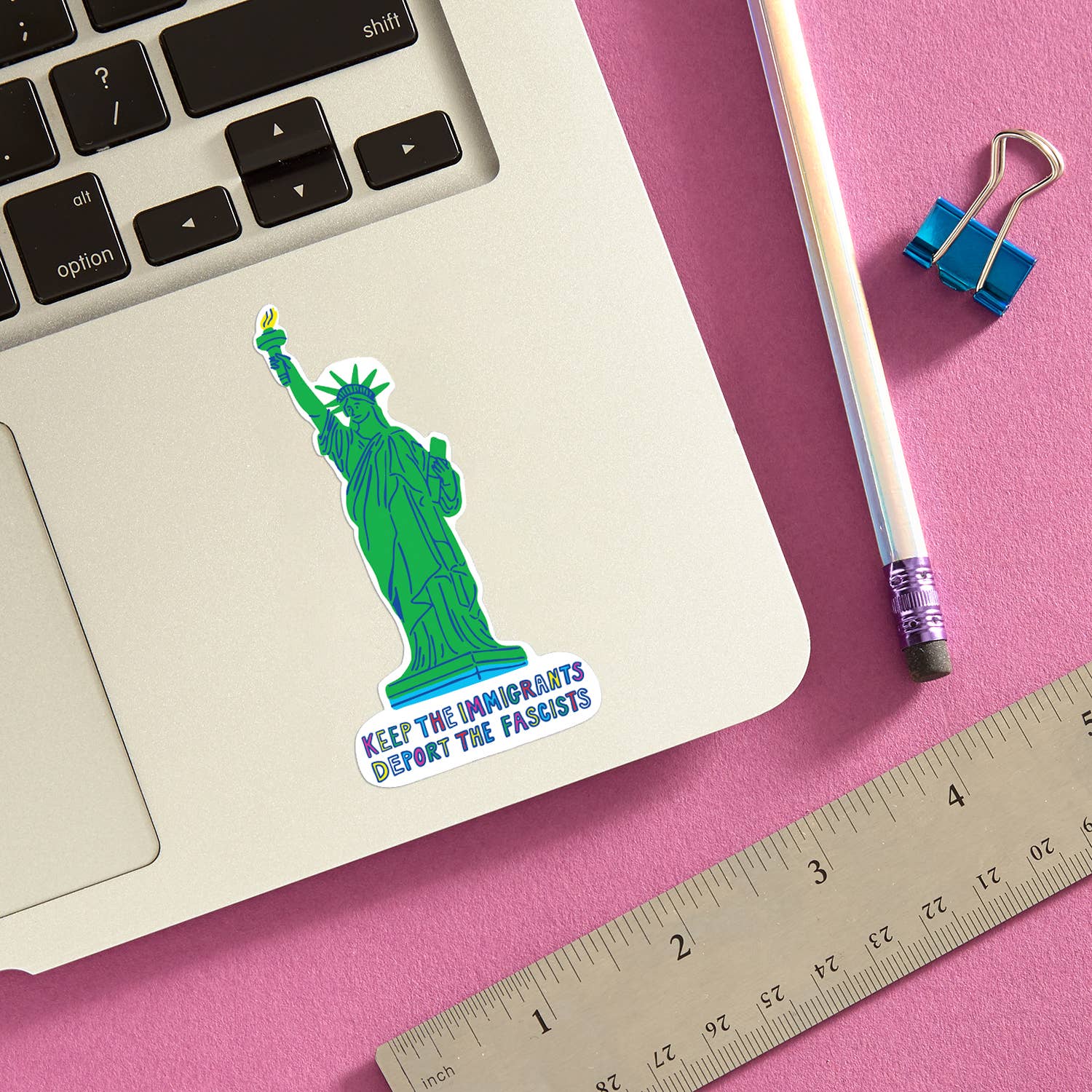 Laptop with a sticker of the Statue of Liberty on a pink surface with a pencil and ruler.