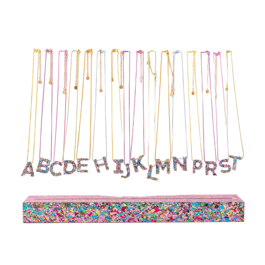 Initial confetti necklaces with colorful chains lined up on a clear and confetti designed display with a white background.