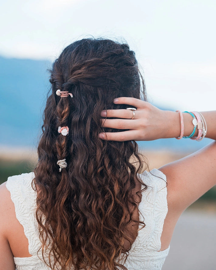 Woman with long, wavy hair wearing decorative hairpins, standing against a blurred natural background.