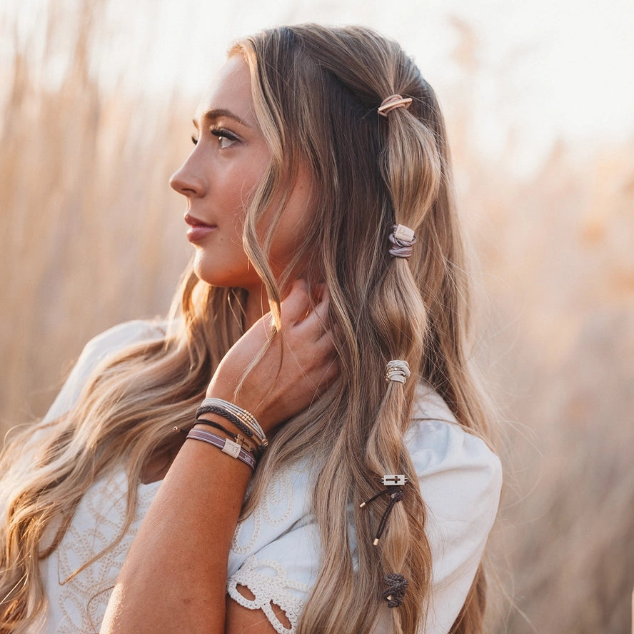 Woman with styled hair in a field, wearing bracelets.