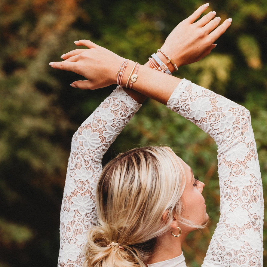 Woman in a white lace dress with arms raised outdoors