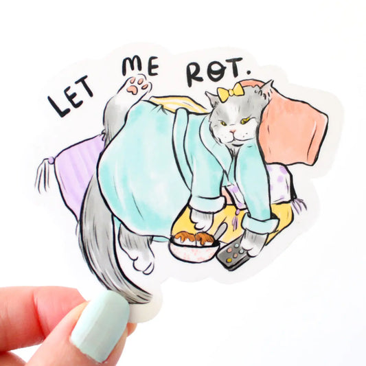 Sticker of a cat in pajamas laying on pillows, remote and snack bowl in paws, with 'Let Me Rot' text, held by a hand.