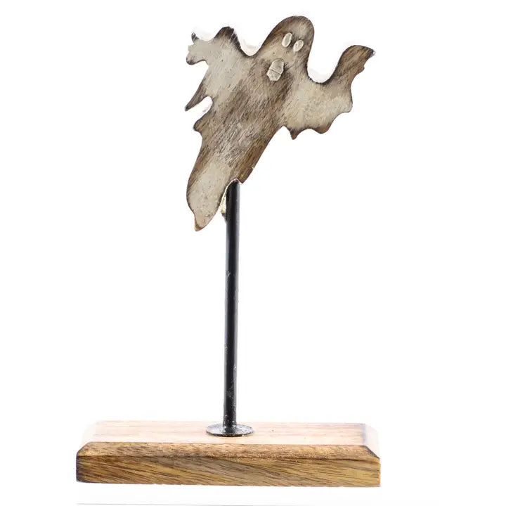 A rustic ghost-shaped metal wall decor piece with a weathered wood-grain finish, mounted on a black metal pole that sits on a rectangular wooden base, shown against a plain white background.