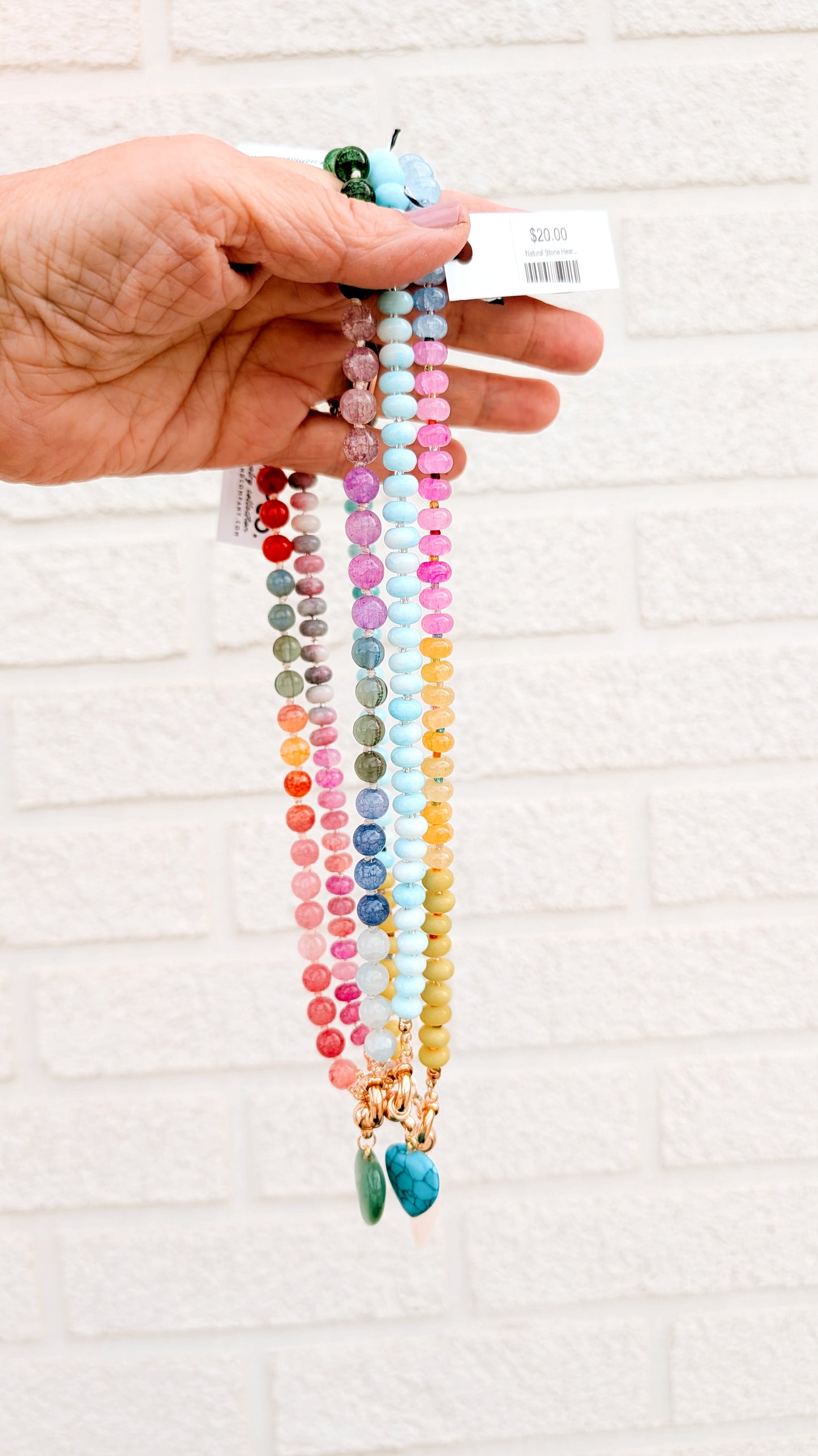 Hand holding a colorful beaded necklace against a white brick wall.