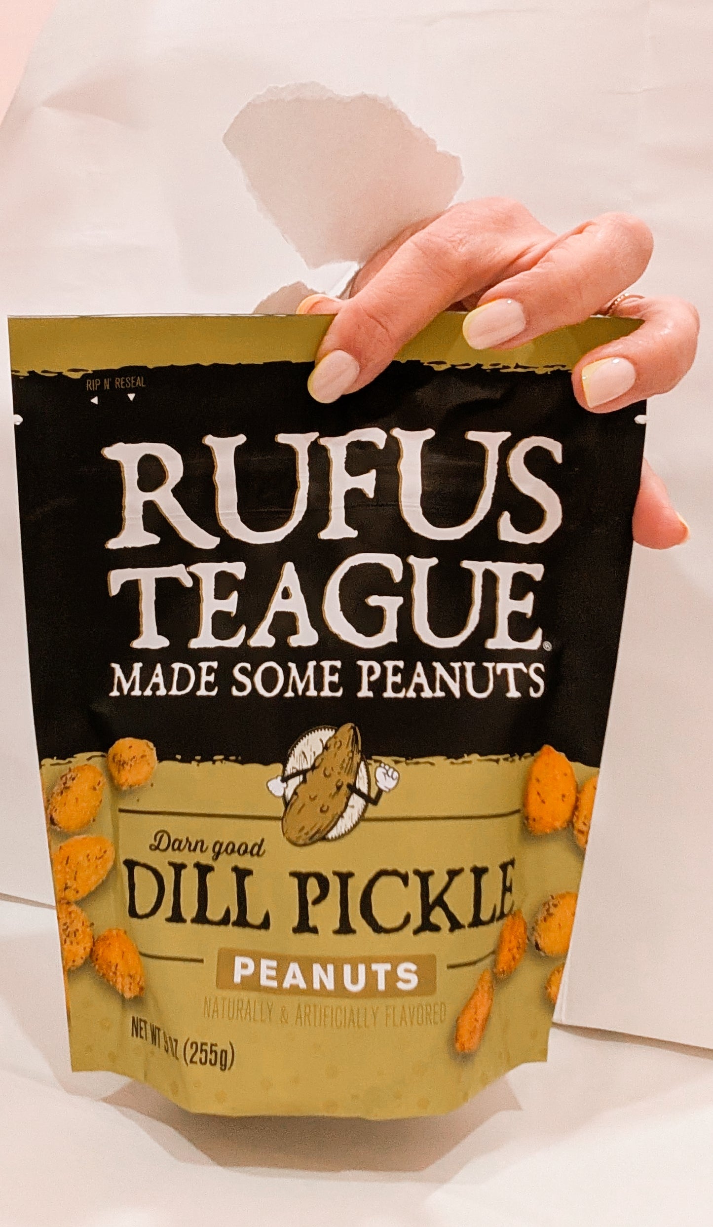 Hand holding a bag of Rufus Teague Dill Pickle flavored peanuts.
