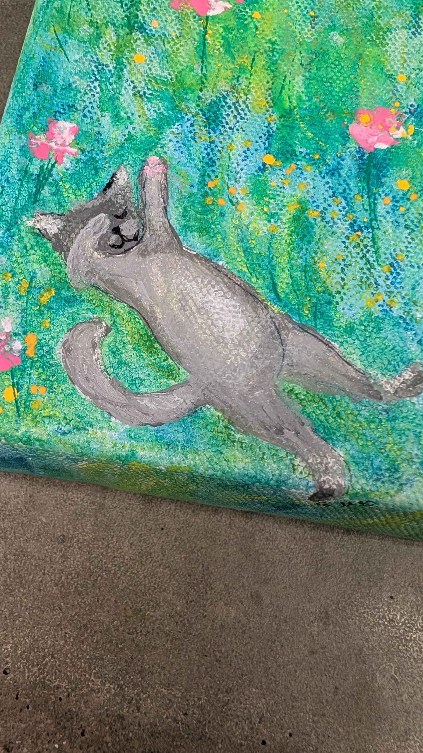 Painted rock with a gray cat and floral design on a textured surface