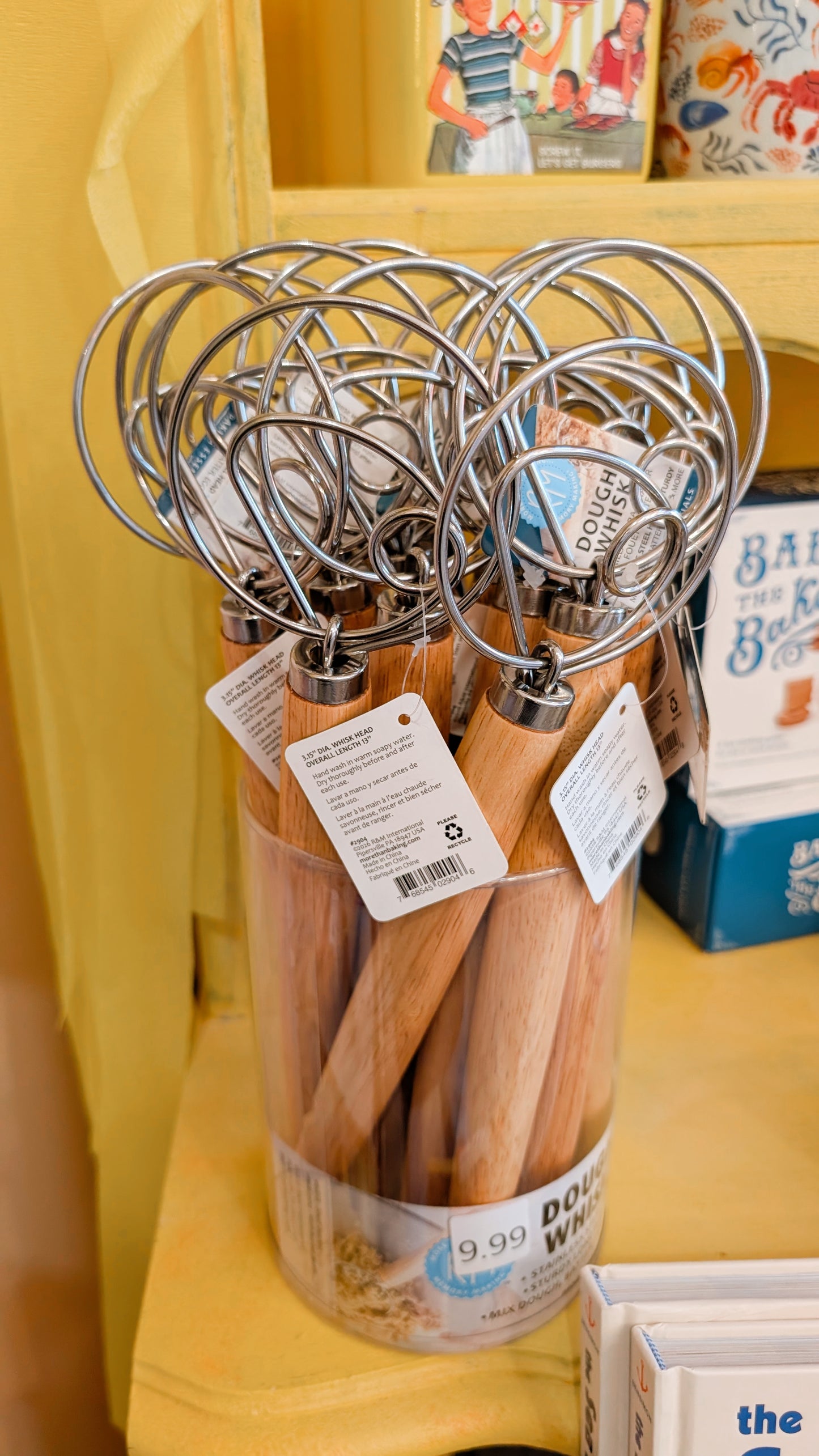 Set of wooden-handled whisks in a container with tags on a yellow surface