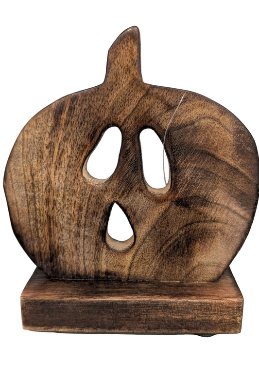 A rustic, handcrafted wooden jack-o'-lantern decoration with carved eyes and mouth, resting on a matching wooden base against a plain indoor background.