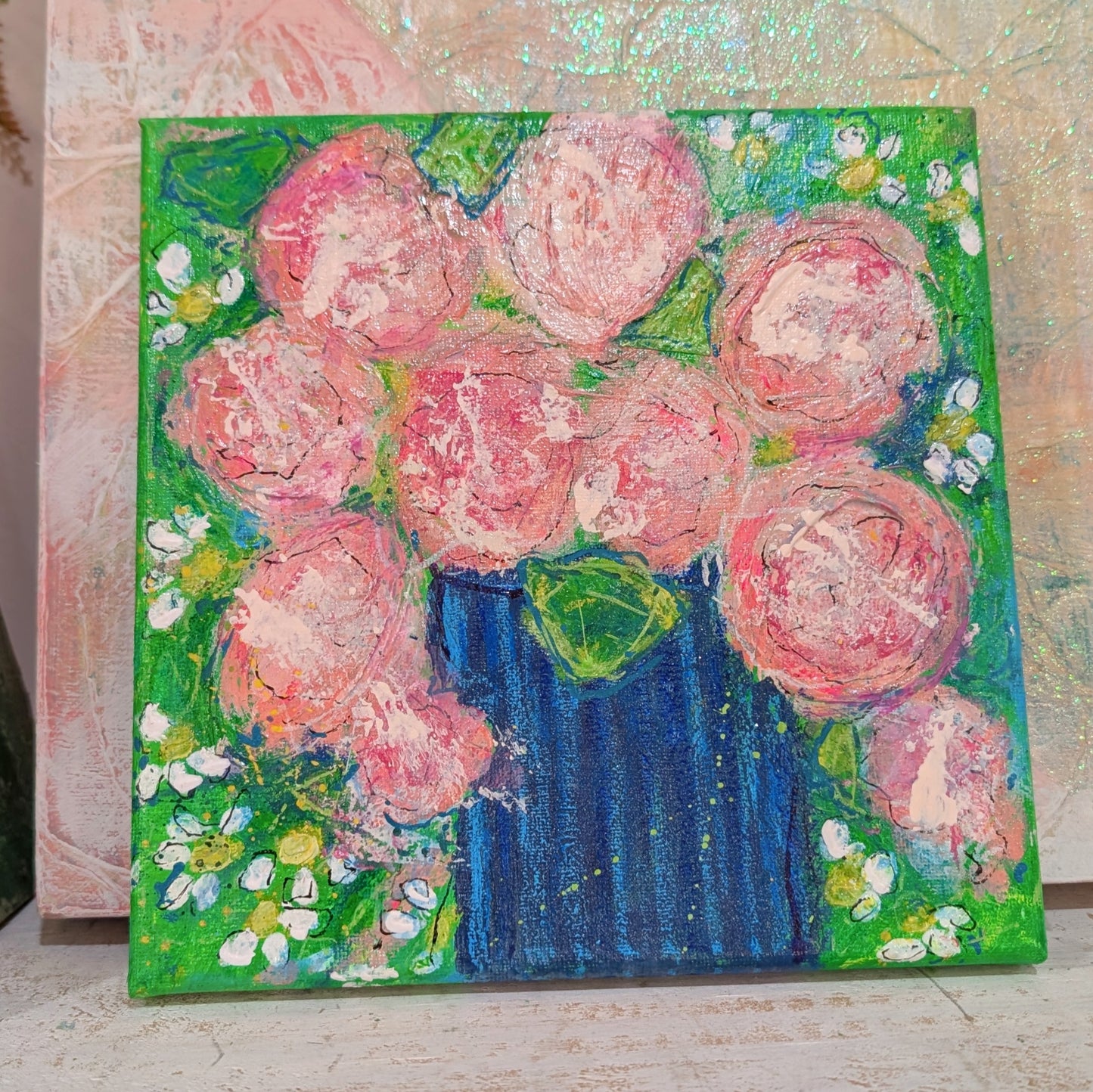 Painting of pink flowers in a blue vase on a textured surface