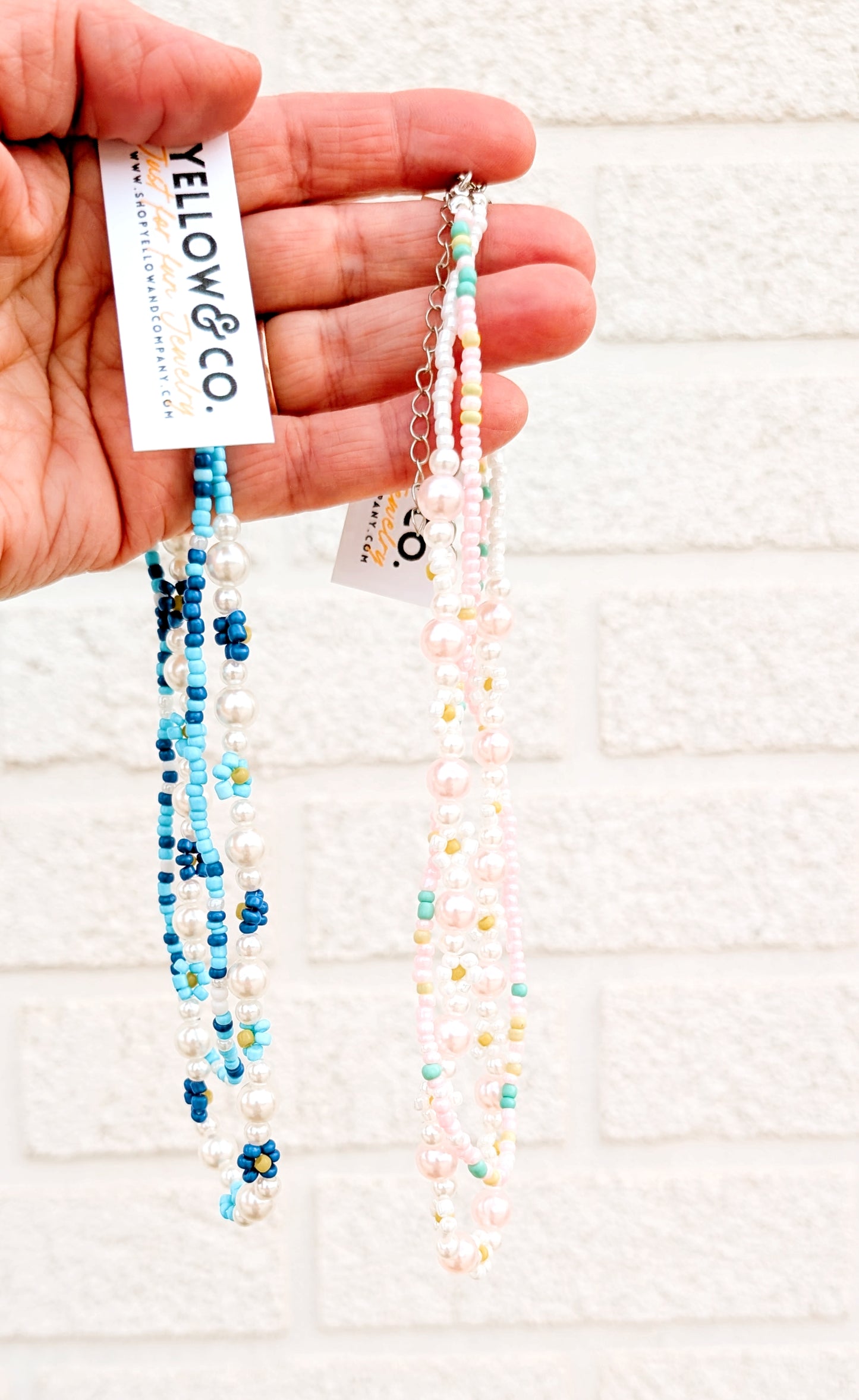 Two beaded necklaces held by a hand with 'Yellow & Co.' tags on a light background