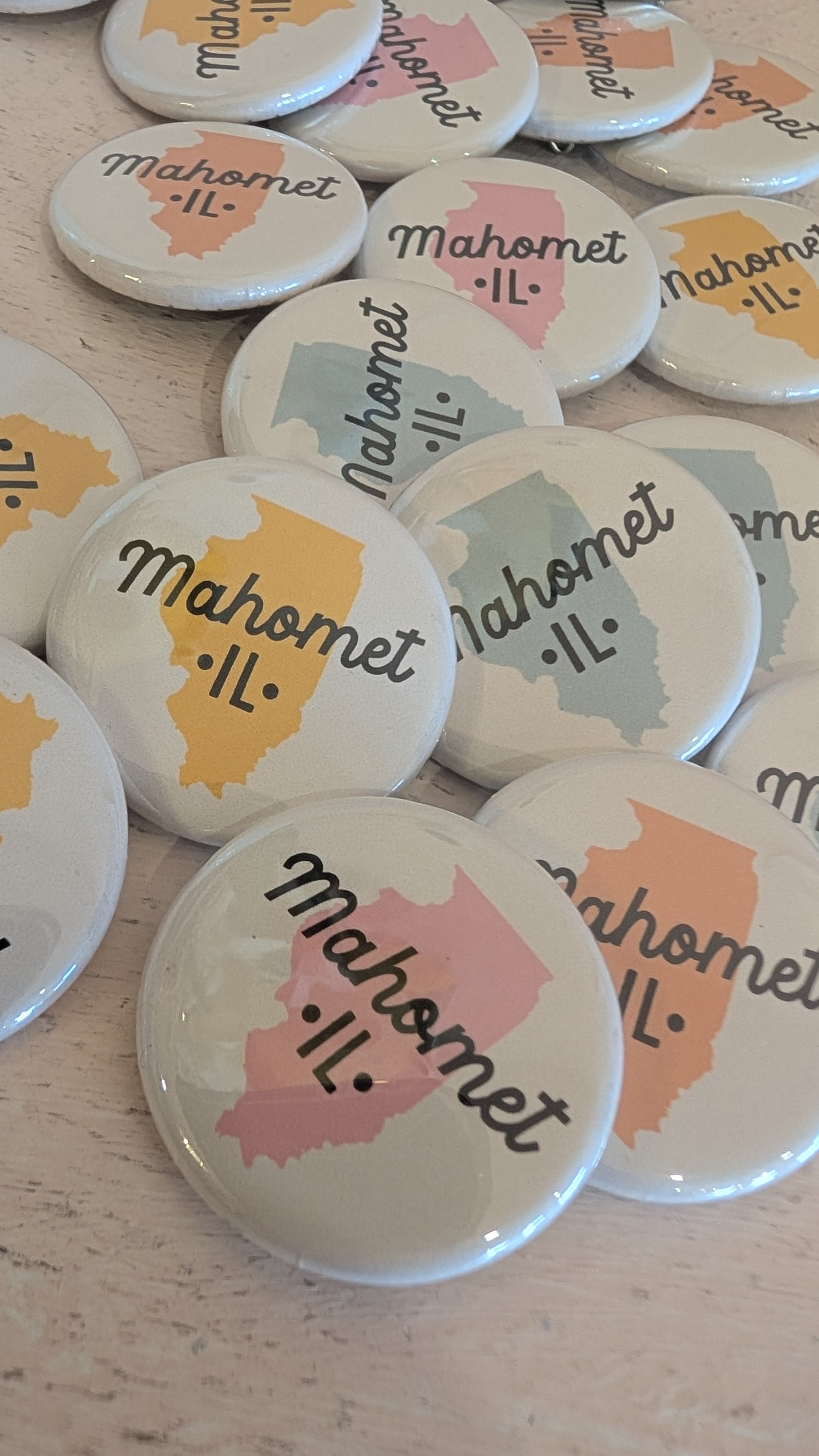 Buttons with 'Mahomet, IL' text and state outline on a wooden surface