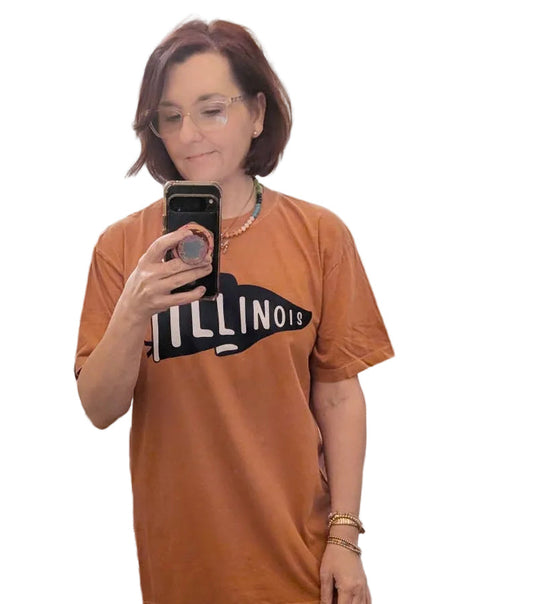 Person wearing a burnt orange t-shirt with text saying Illlinois, taking a mirror selfie in a room.