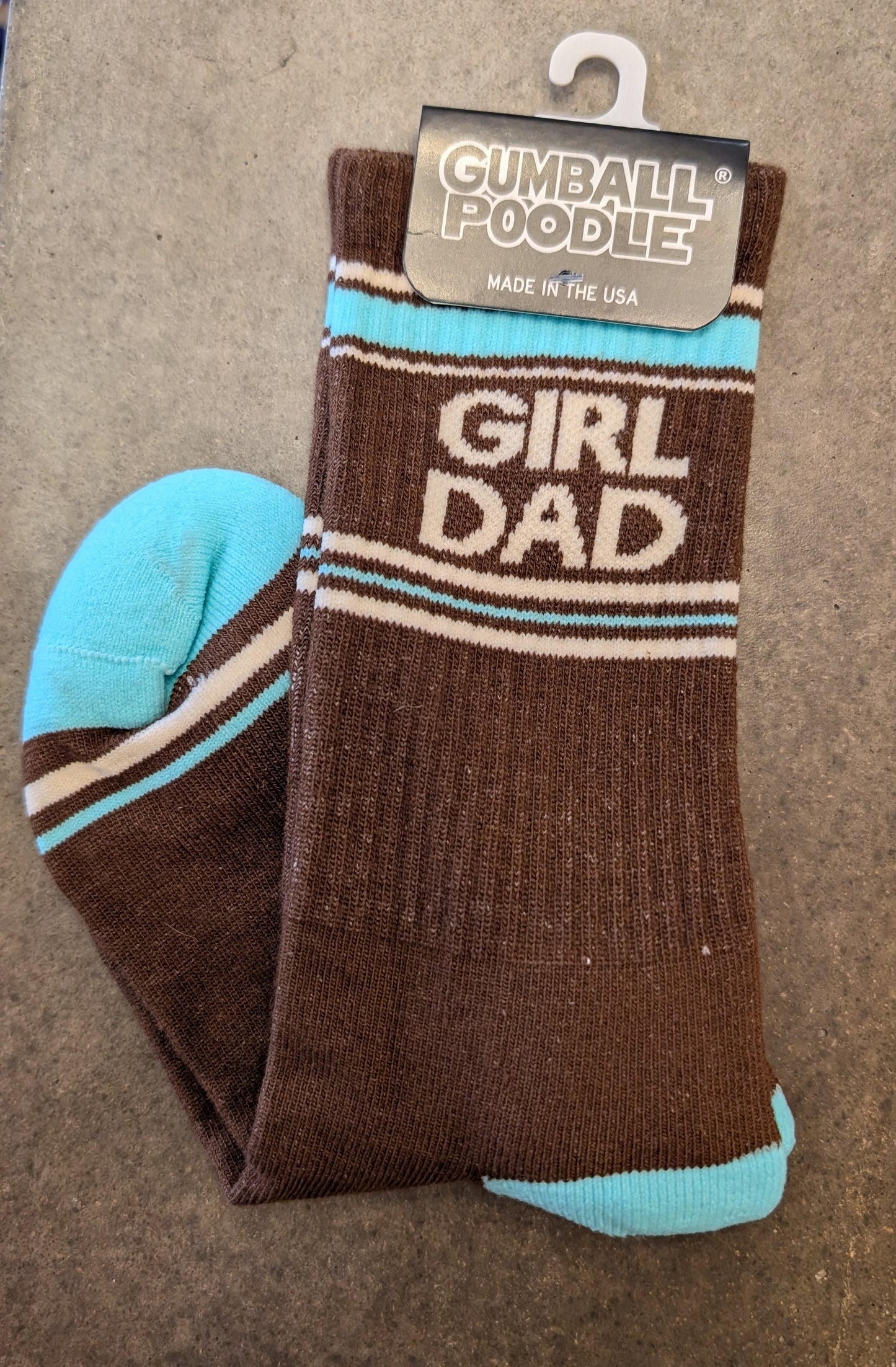 Brown sock with 'Girl Dad' text and blue accents, displayed on a beige surface with a 'Gumball Poodle' tag.