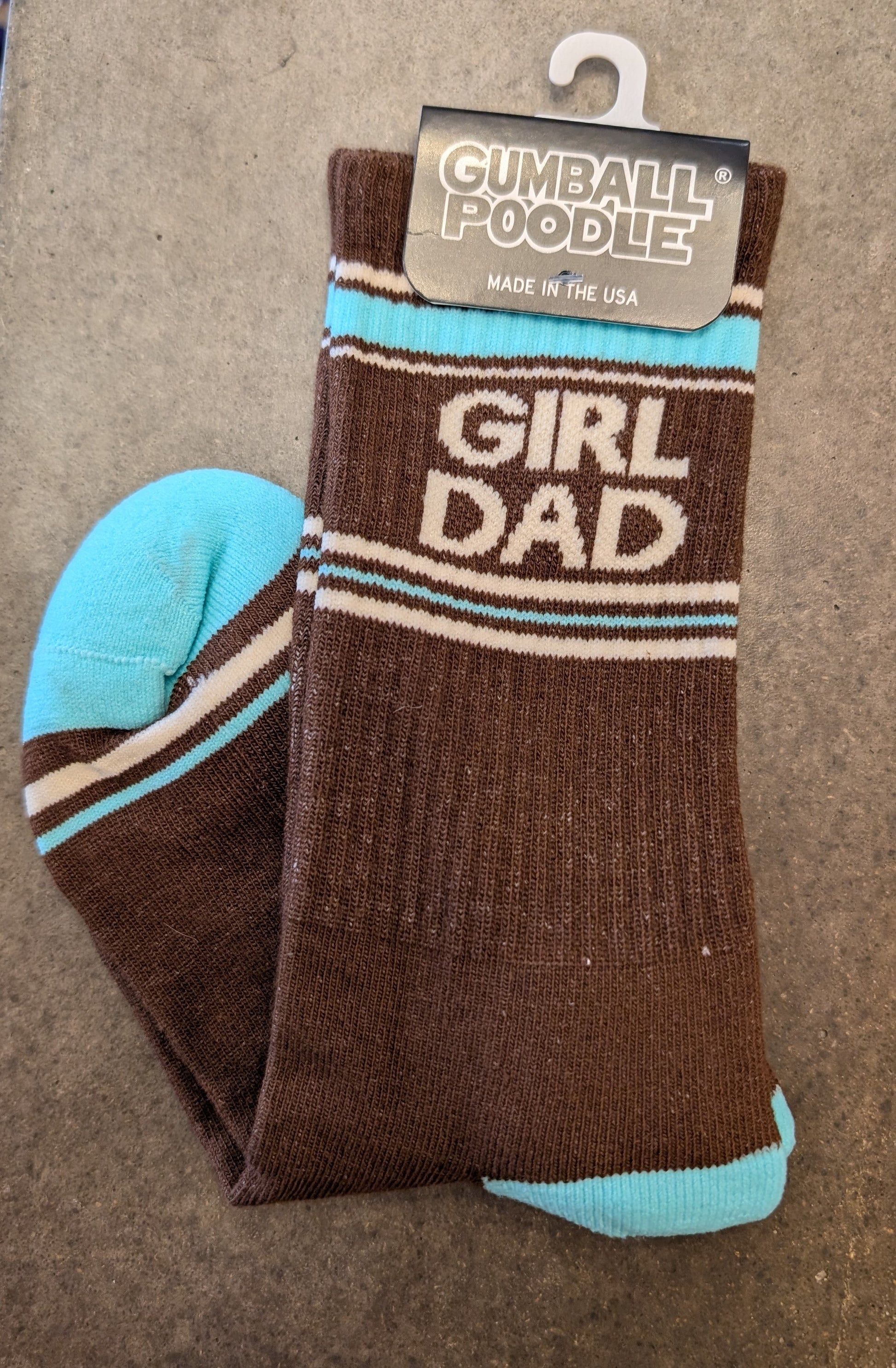 Brown sock with 'Girl Dad' text and blue accents, displayed on a beige surface with a 'Gumball Poodle' tag.