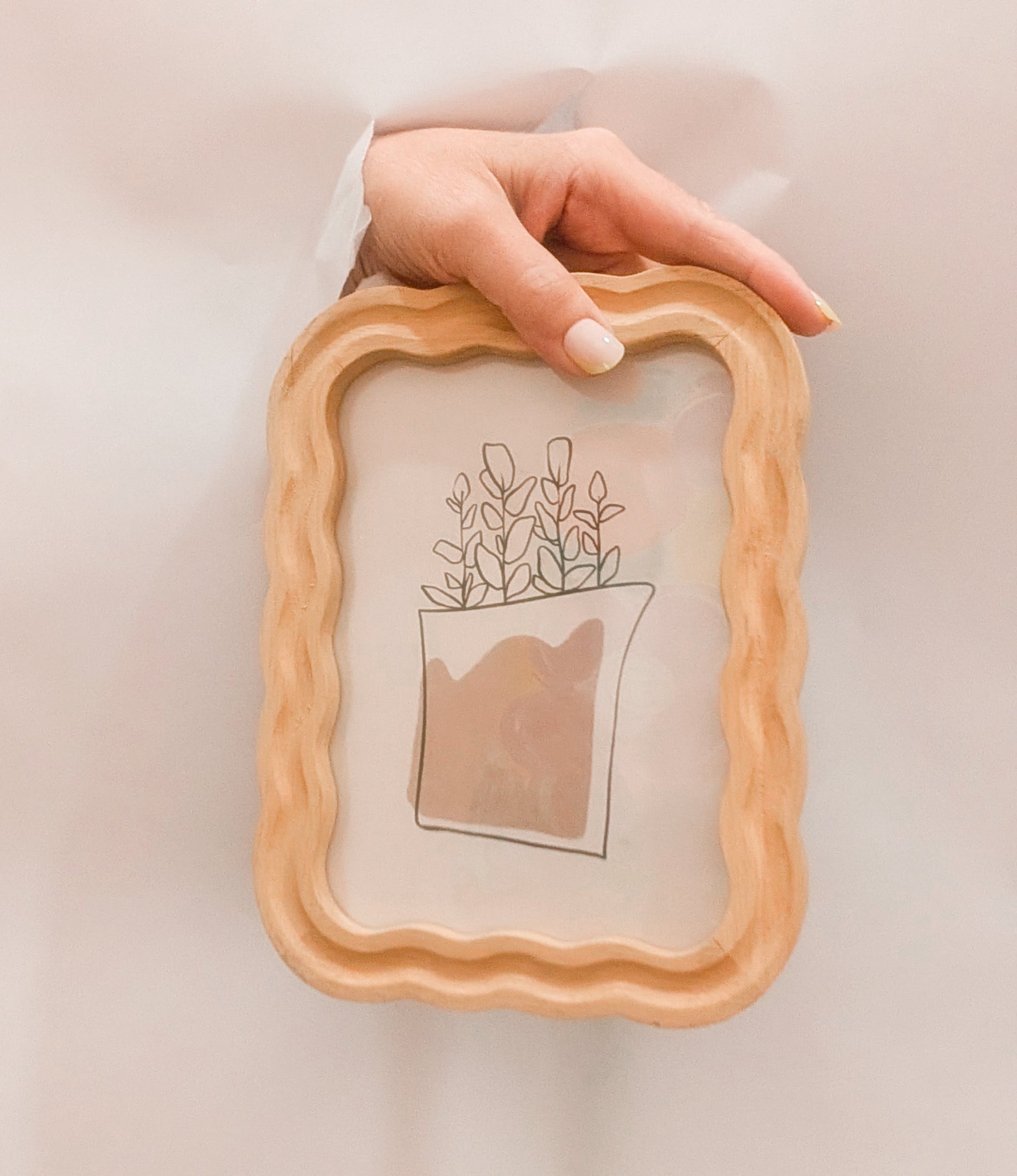 Wooden frame with a plant illustration held by a hand on a light background