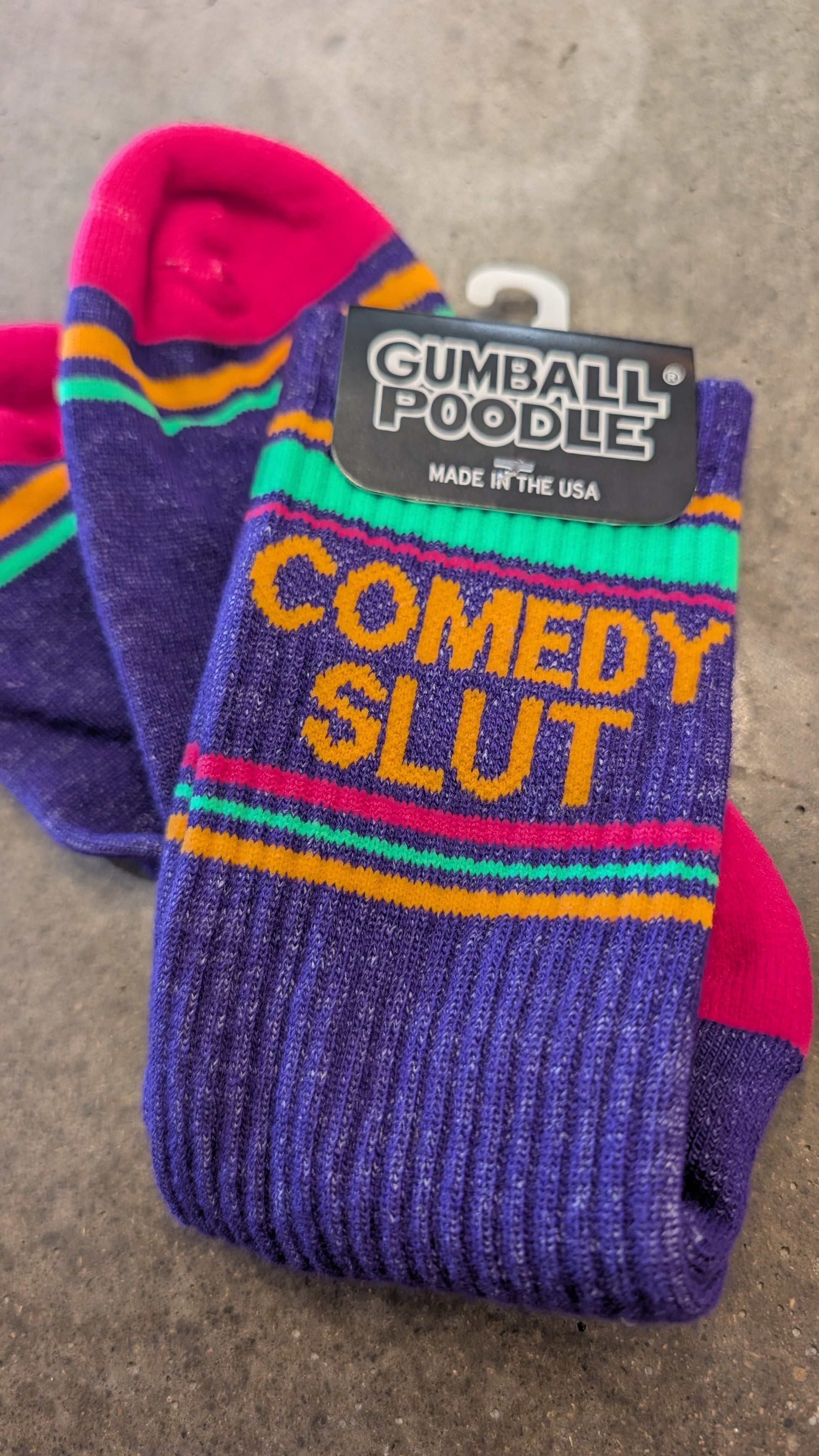 Pair of colorful socks with 'Comedy Slut' text and Gumball Poodle branding on a gray surface.