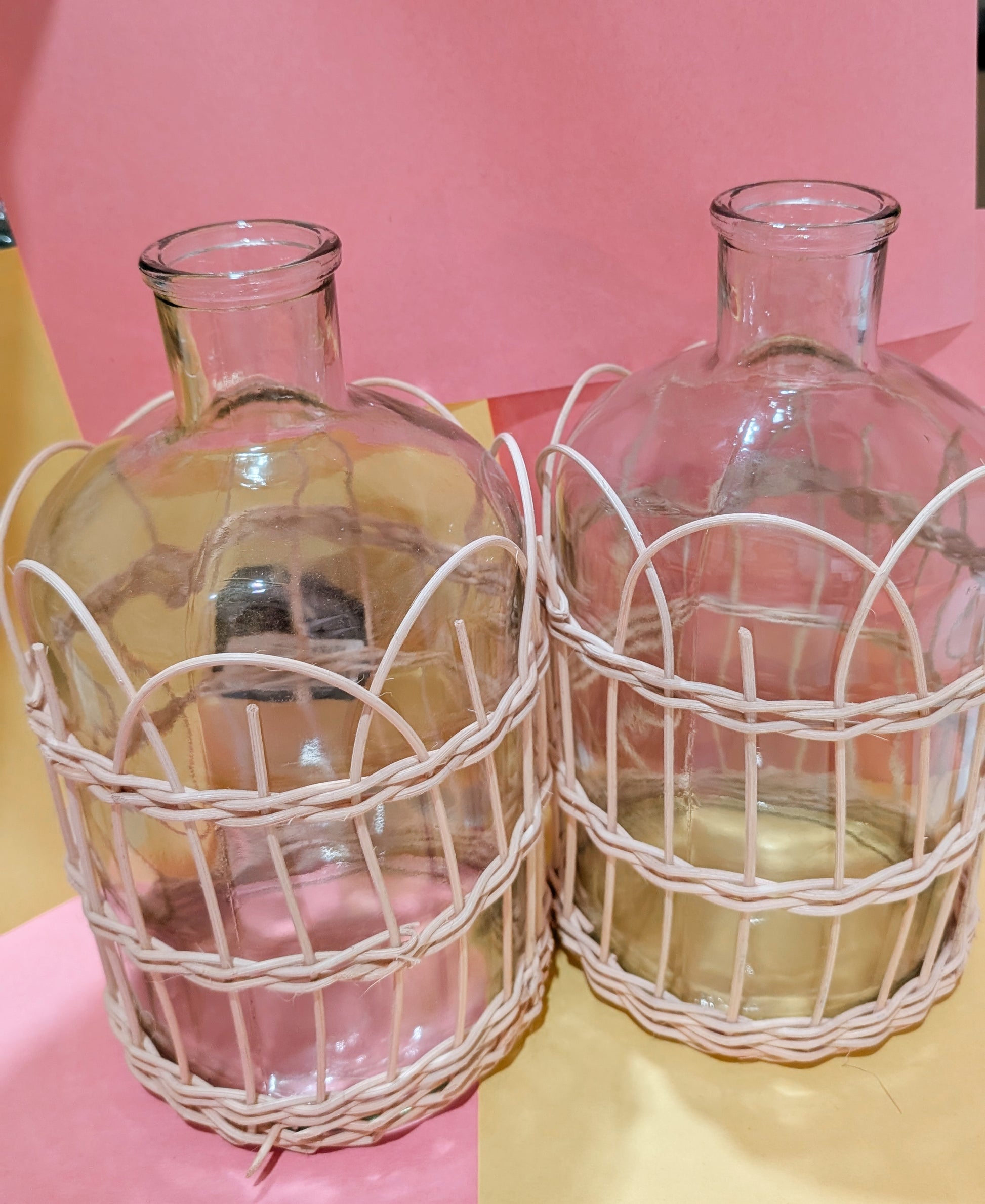 Two glass bottles with wire cages on a pink background