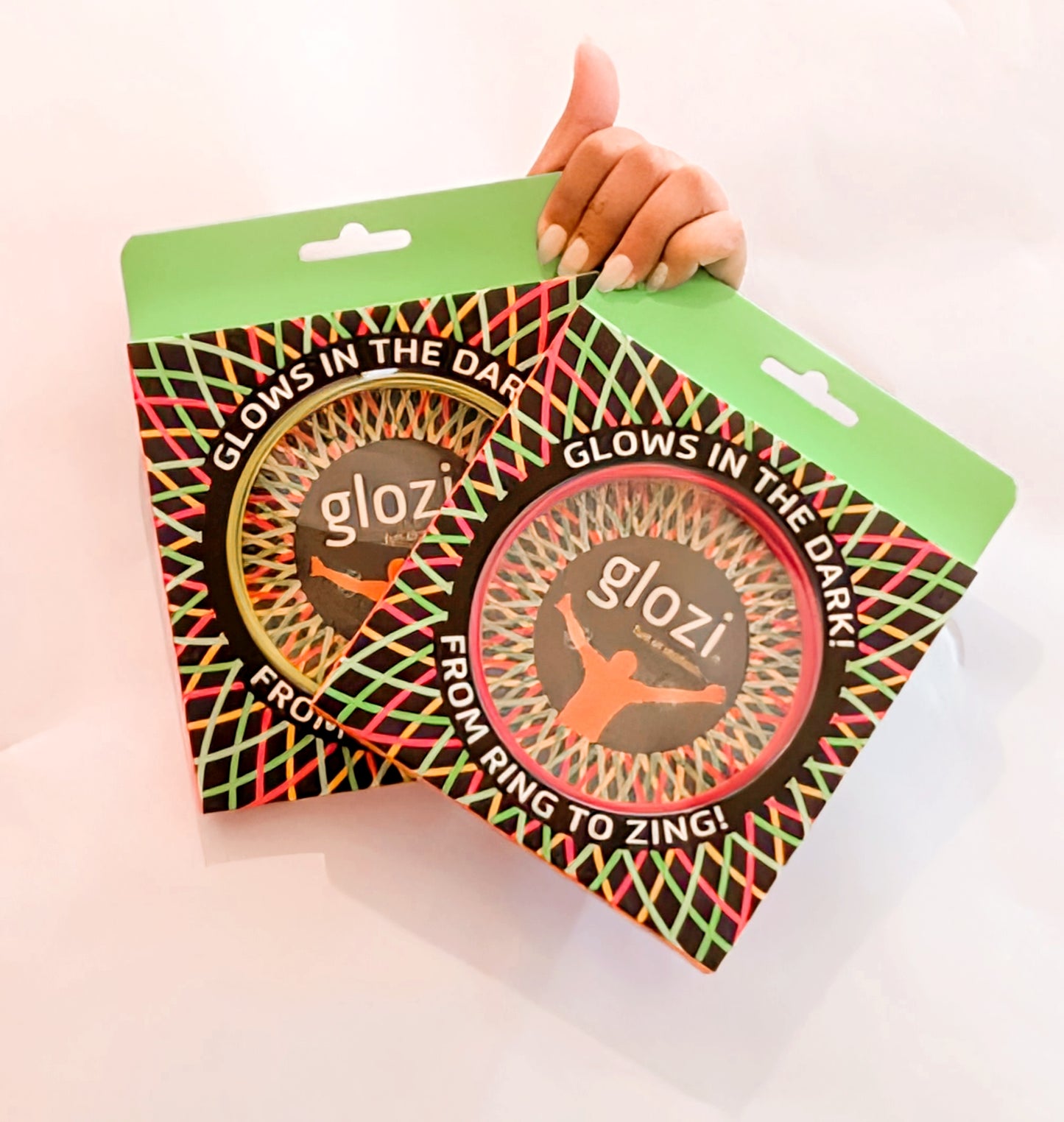 Two packages of glozi products glowing in the dark held by a hand on a light pink background.