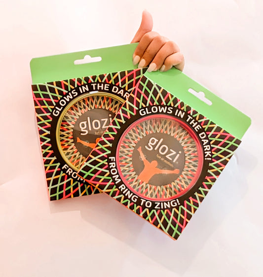 Two packages of glozi products glowing in the dark held by a hand on a light pink background.