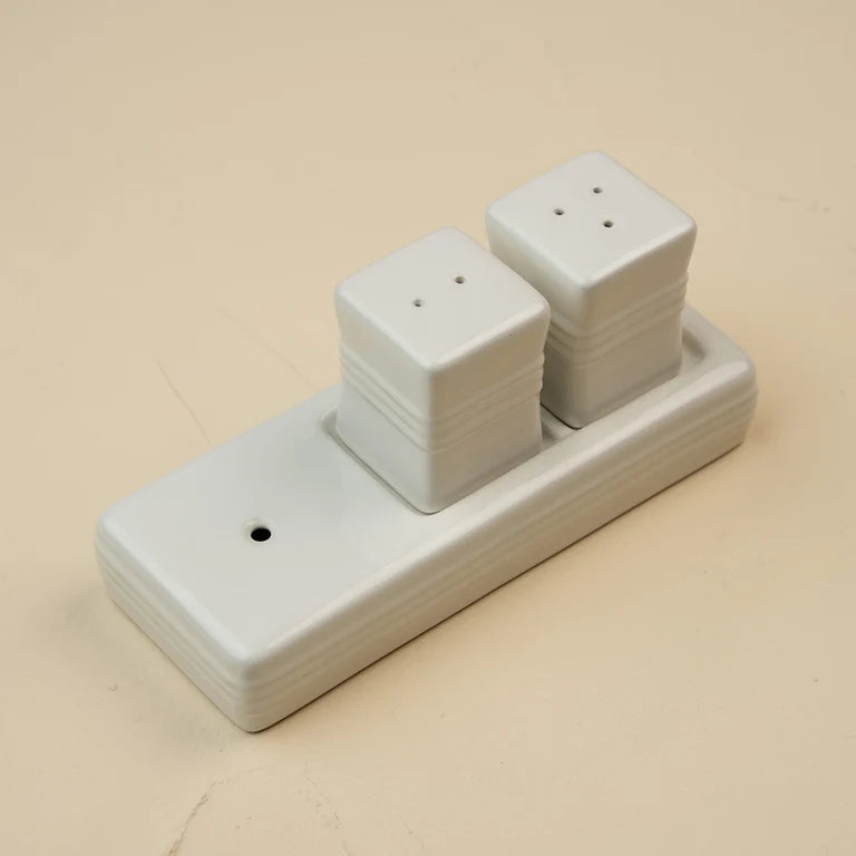 A white ceramic salt and pepper shaker set on a matching rectangular holder, photographed on a plain beige background.